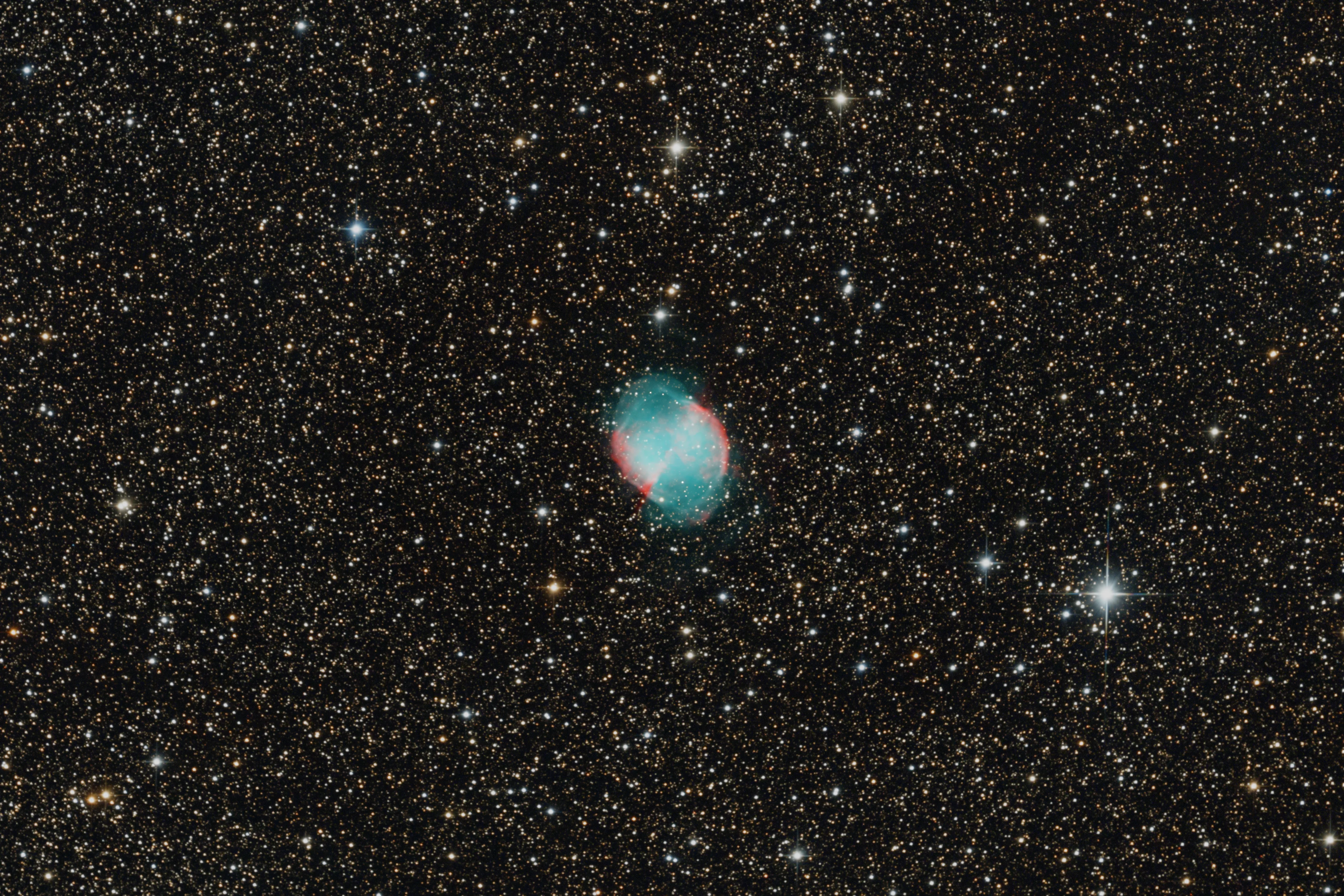 The Dumbbell Nebula glowing blue-green and red among many stars