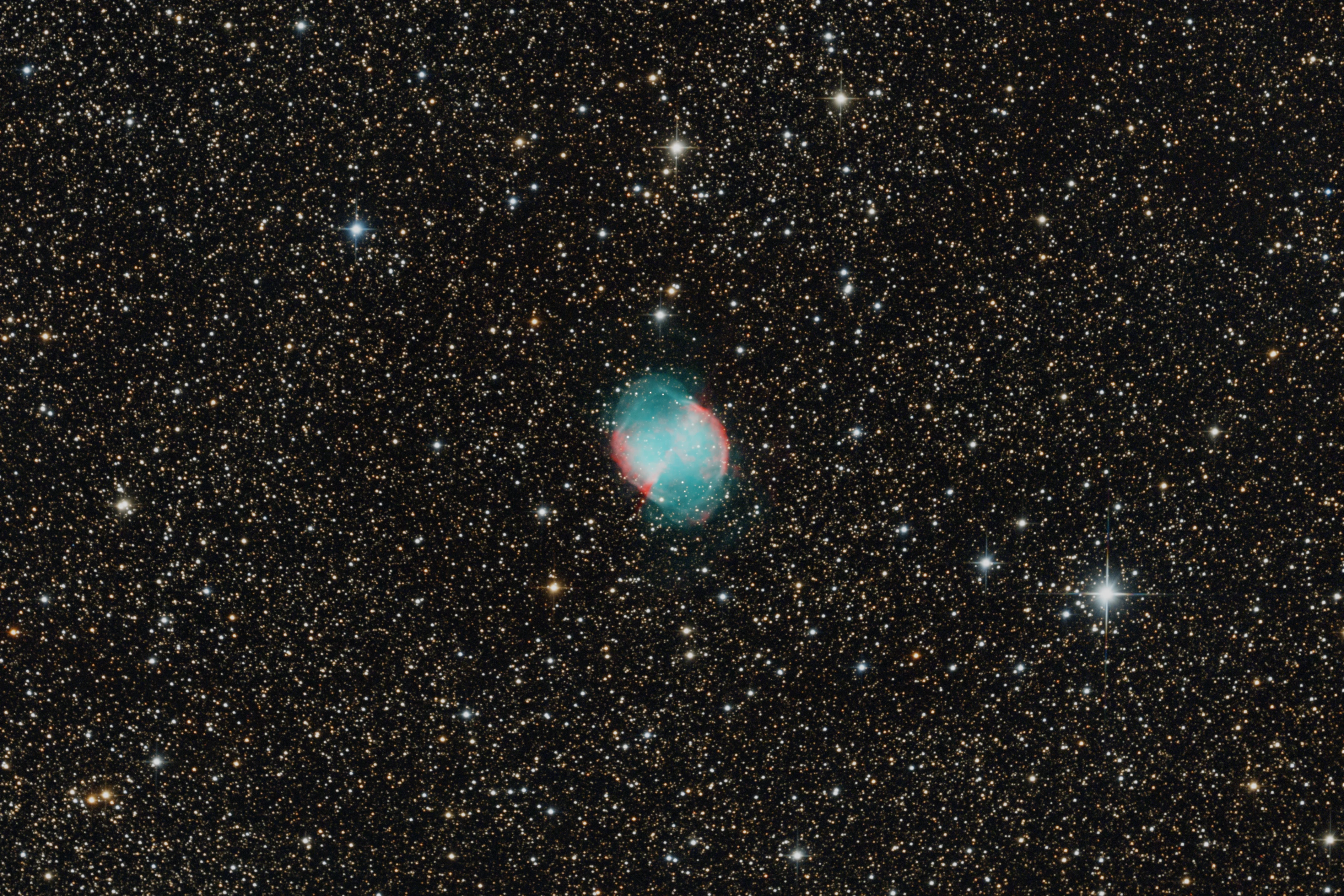 The Dumbbell Nebula glowing blue-green and red among many stars